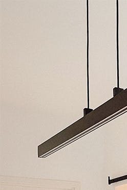 Des bougies décoratives, un vase de fleurs séchées sur une table à manger en bois éclairée par une longue lampe minimaliste