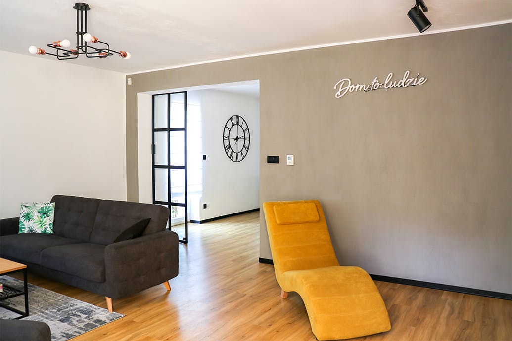 salon ouvert, canapé gris dans le salon, lampe industrielle dans le salon, fauteuil jaune pour le salon, mur gris dans le salon, salon ouvert sur salle à manger, porte métallique vitrée, porte coulissante vitrée, mezzanine porte de style, enseigne au néon sur le mur, décorations au néon