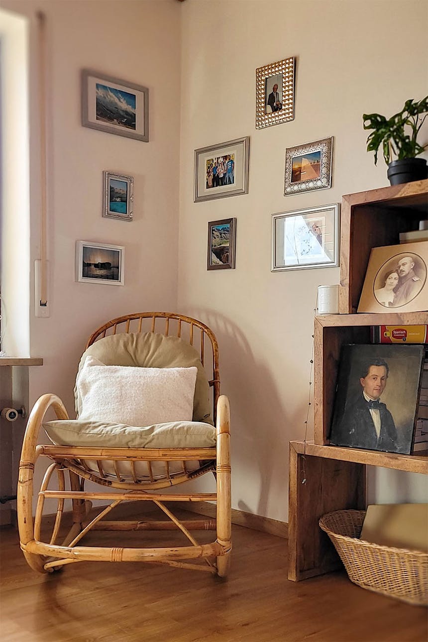 ein Schaukelstuhl aus Korbgeflecht an einer mit einer Fotogalerie geschmückten Wand