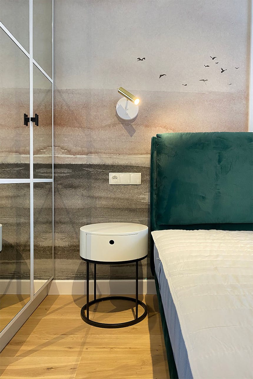 mały biały stolik nocny na tle dekoracyjnej tapety w sypialni nowoczesnego mieszkania