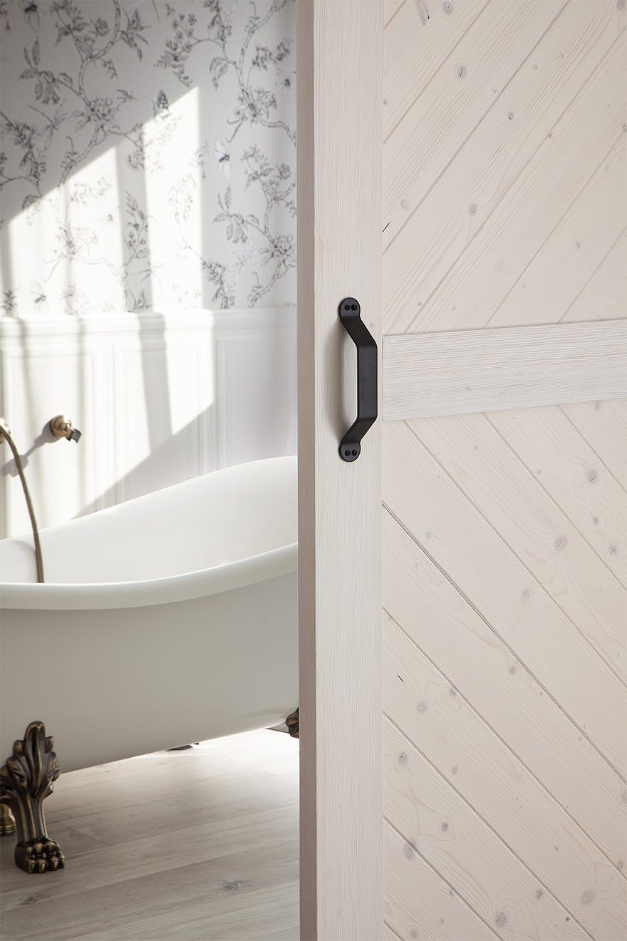 an open white wooden door revealing a fragment of a bathroom with a free-standing bathtub
